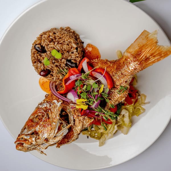 Whole fried snapper with rice and beans, topped with colorful vegetables and herbs.