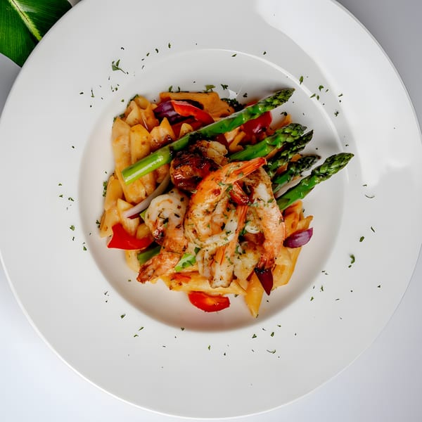 Grilled shrimp and asparagus served over pasta with red peppers and onions on a white plate.