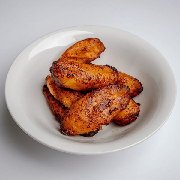A white bowl filled with several pieces of golden-brown, caramelized fried plantains.