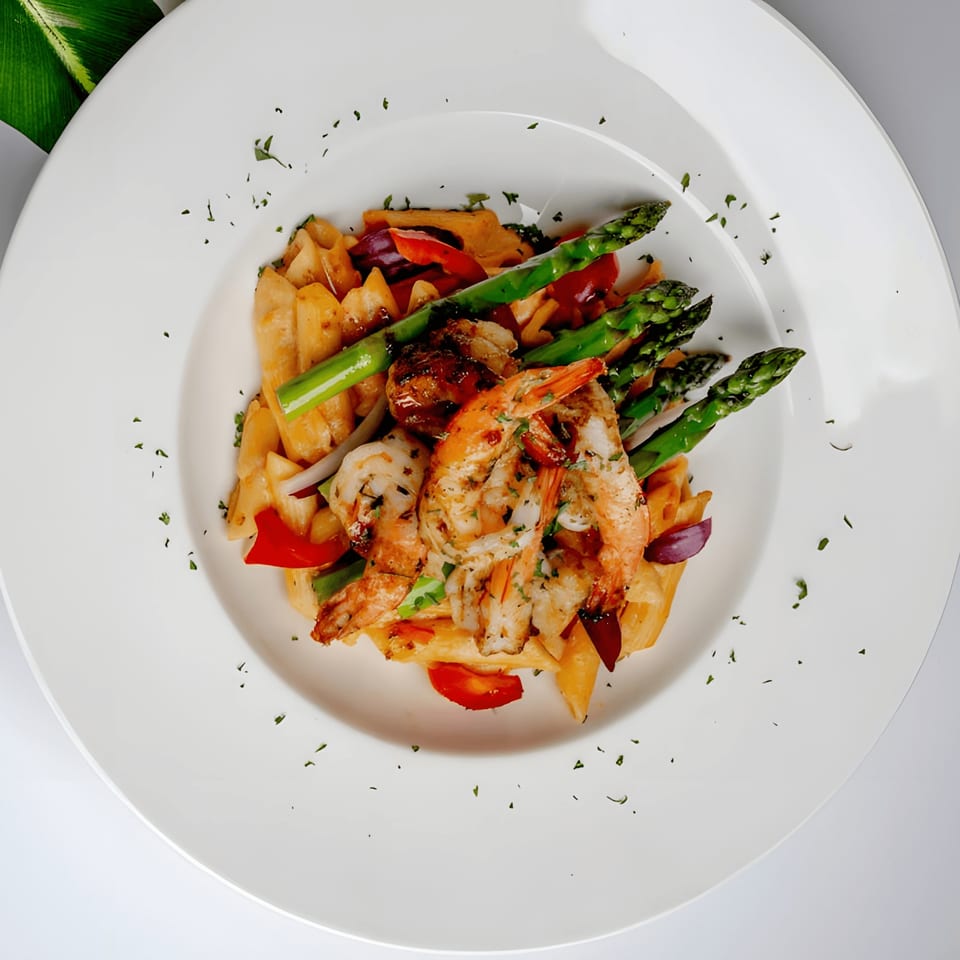 Caribbean shrimp pasta with asparagus, red peppers, and onions on a white plate.