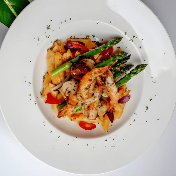 Caribbean shrimp pasta with asparagus, red peppers, and onions on a white plate.