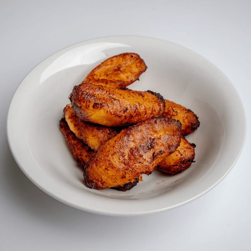 A white bowl filled with several pieces of golden-brown, caramelized fried plantains.