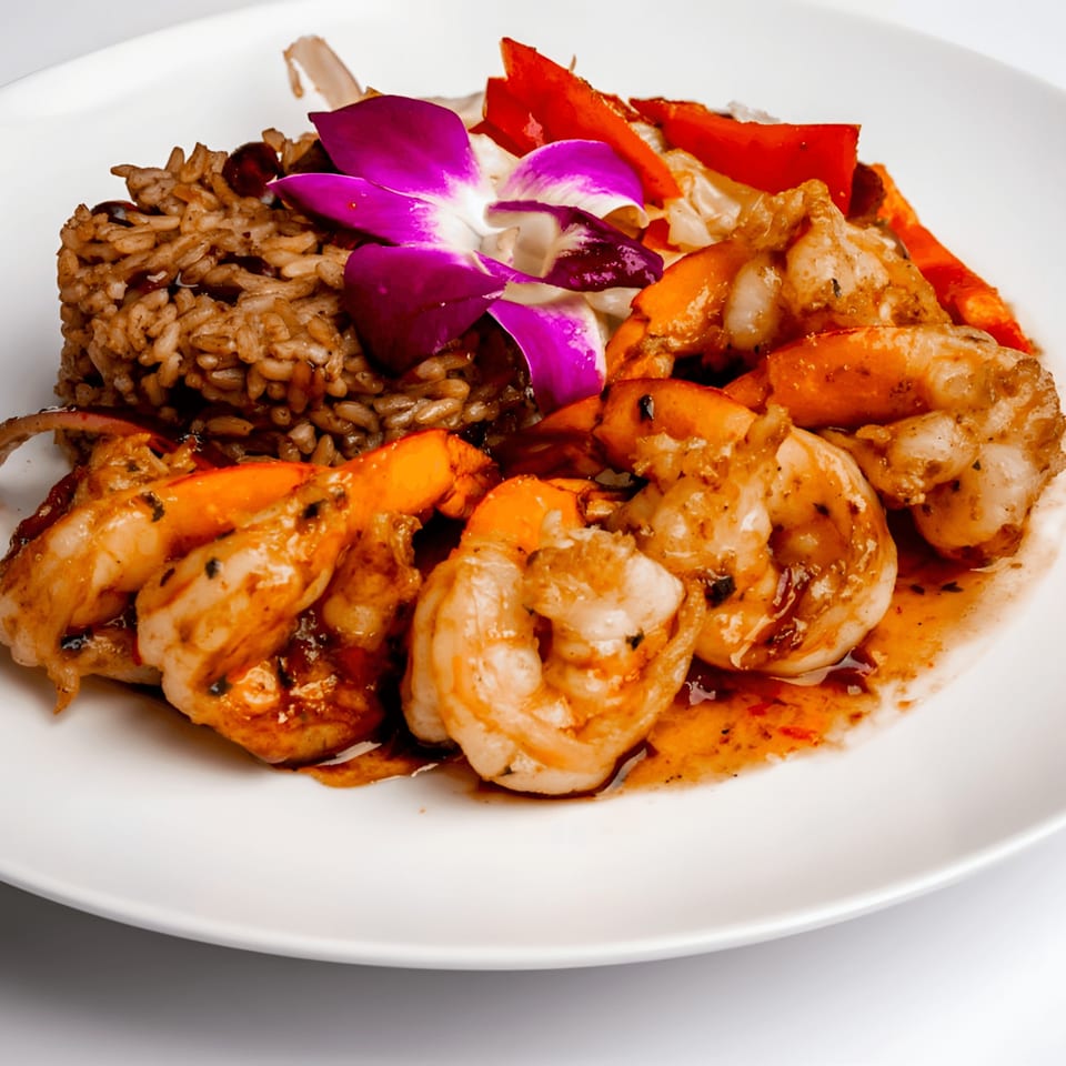 Caribbean shrimp dish with rice, red peppers, and a purple orchid garnish on a white plate.