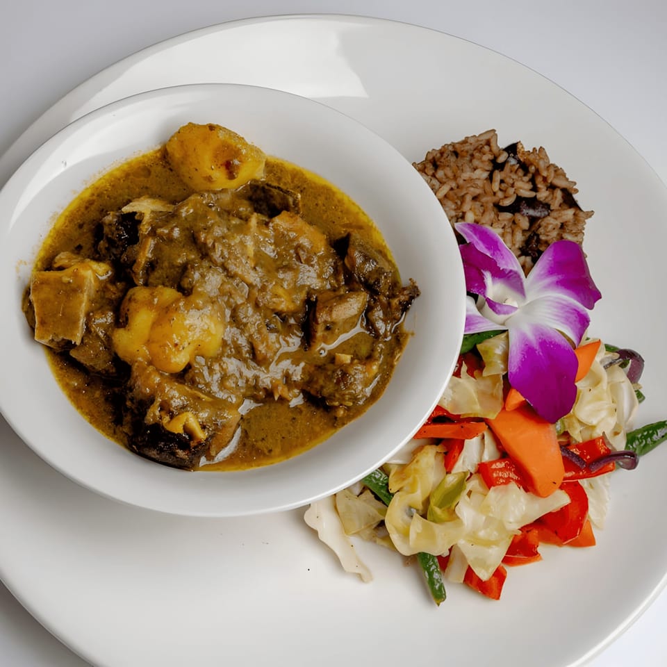 A bowl of Caribbean curry with potatoes, rice, and mixed vegetables, garnished with an orchid.